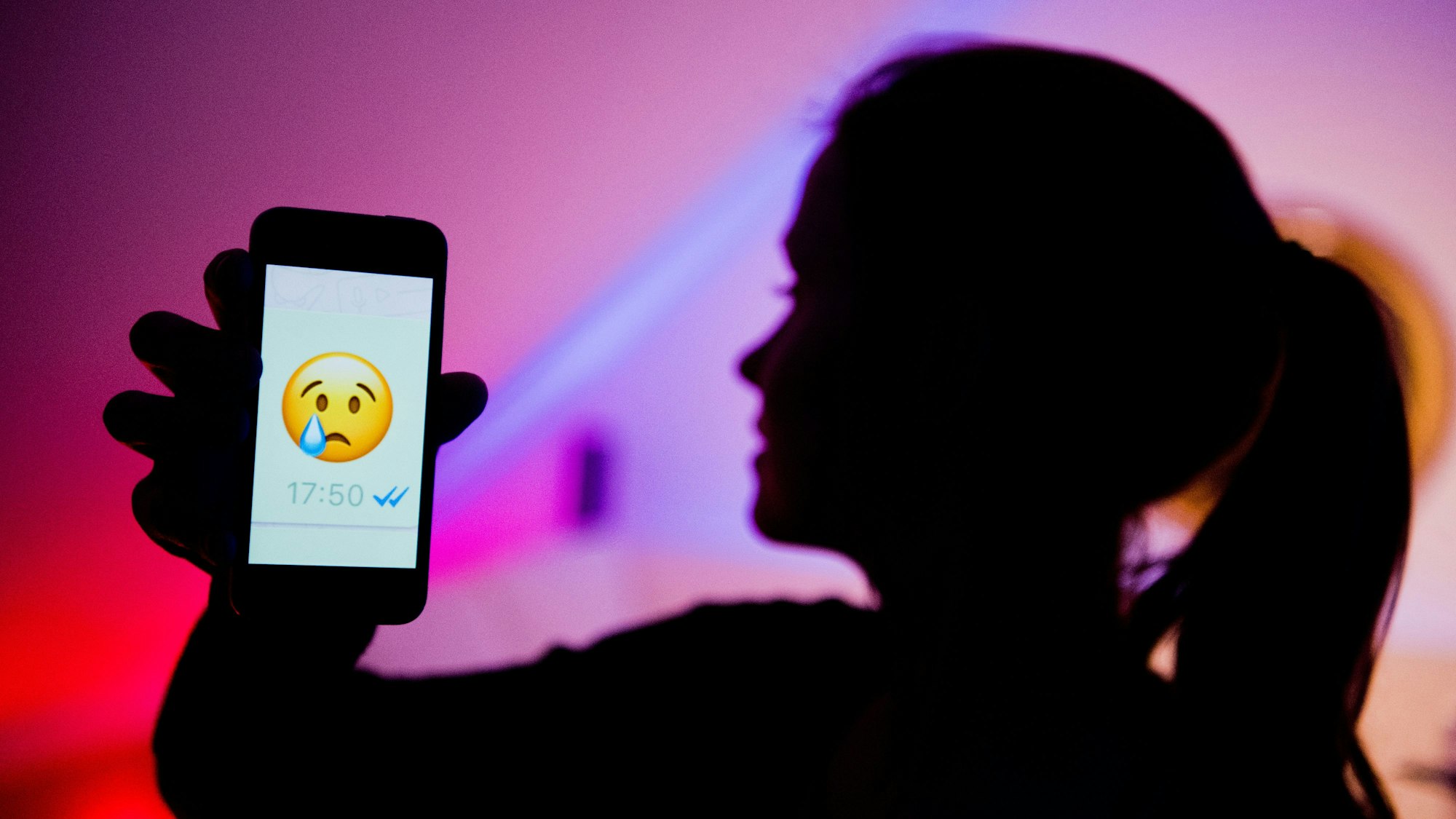 Ein junges Mädchen zeigt das Display eines Smartphones mit einem weinenden Emoji beim Messenger ‚WhatsApp‘ (gestellte Szene).