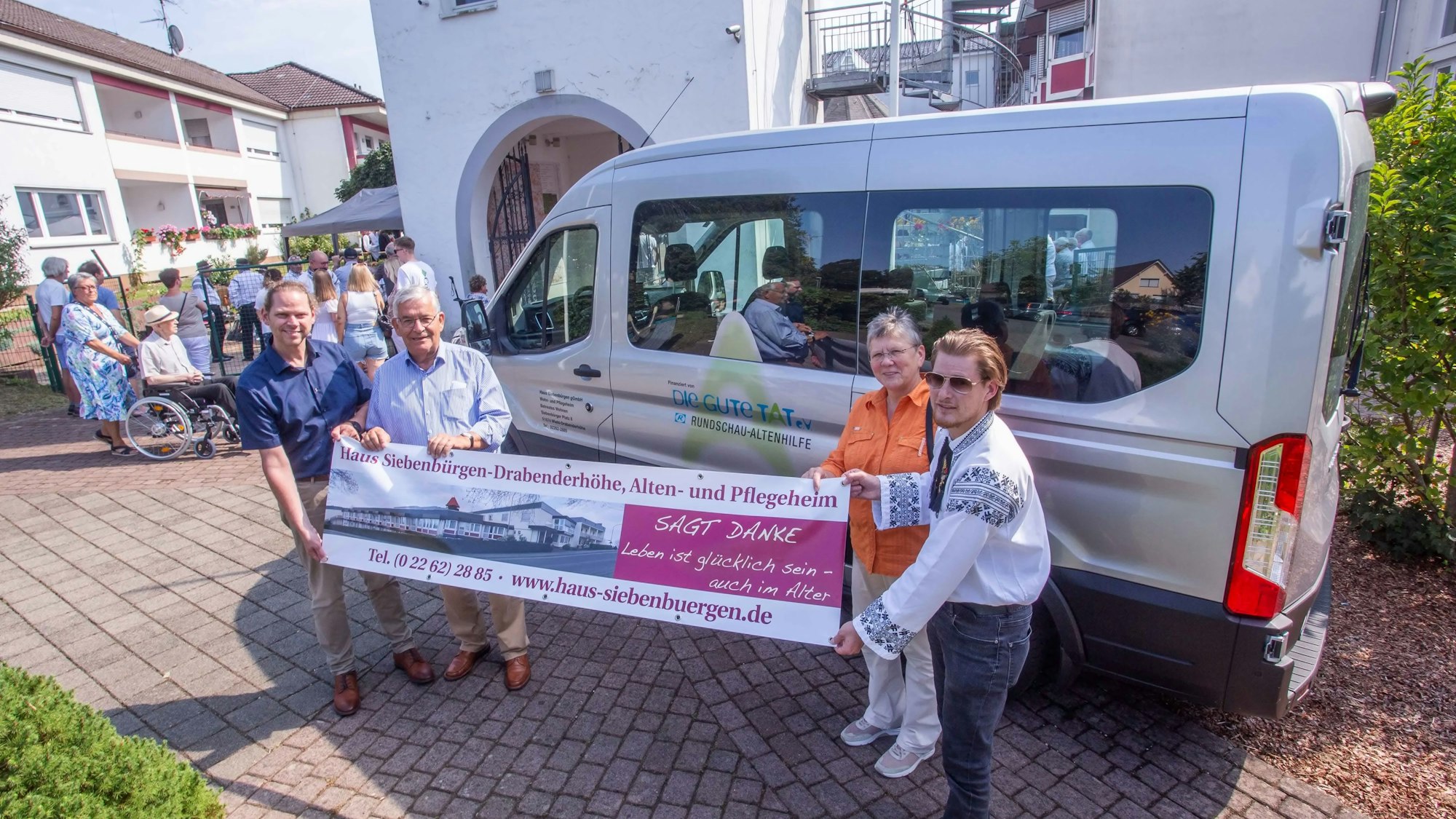 Vier Personen halten ein Dankeschön-Transparent vor einen Kleinbus.