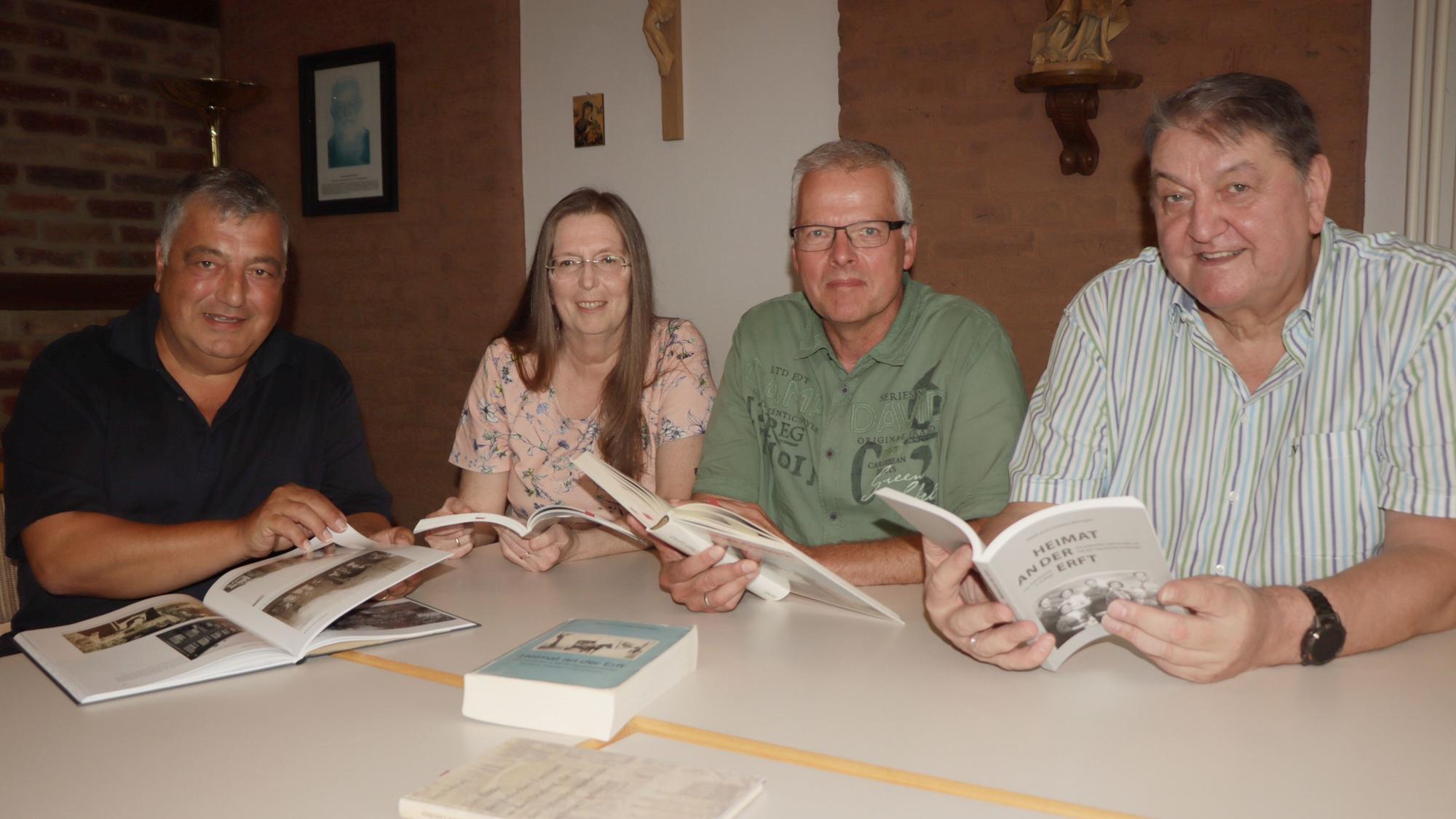 Die Mitglieder des Rechercheteams sitzen an einem Tisch und halten jeweils ein Buch aufgeschlagen vor sich. Sie schauen in die Kamera. Auf dem Tisch liegt ein weiteres Buch.