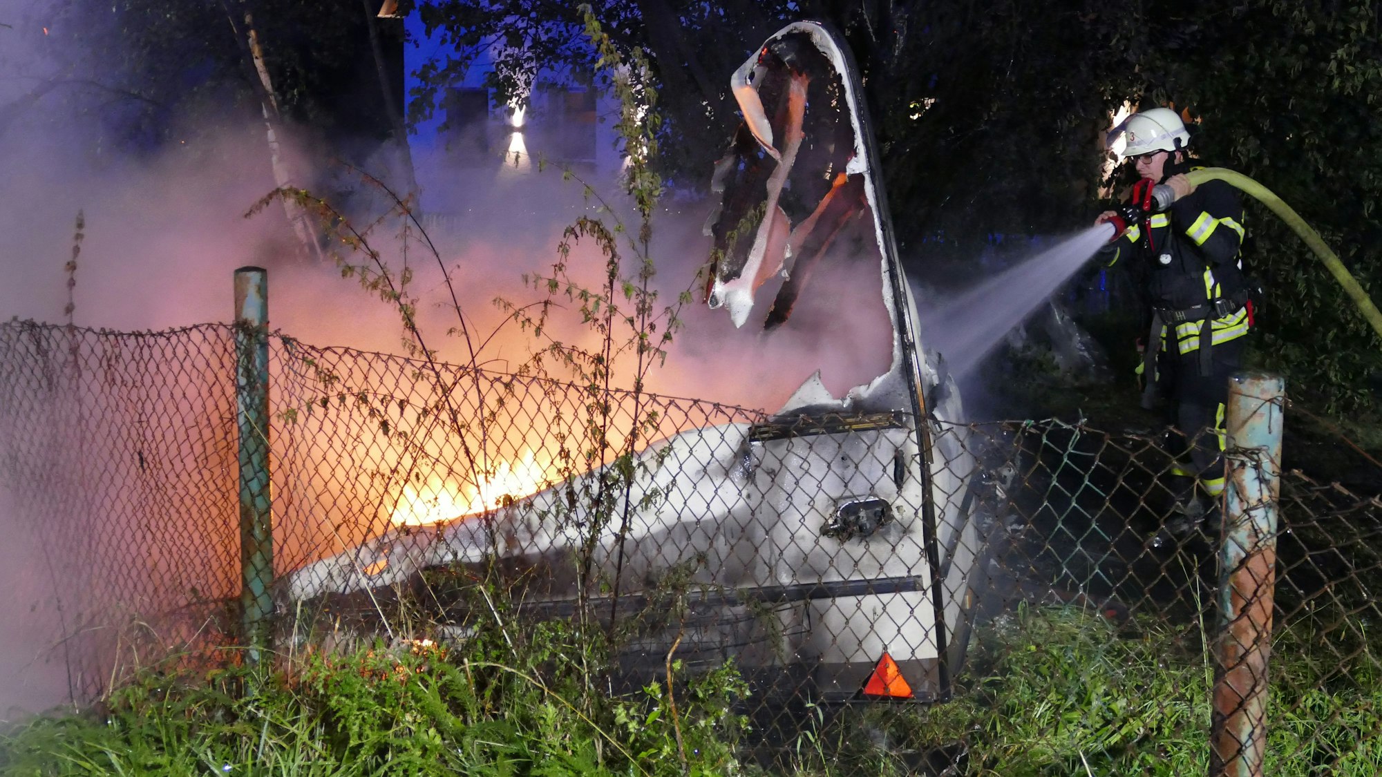 Ein Feuerwehrmann löscht einen brennenden Wohnwagen.
