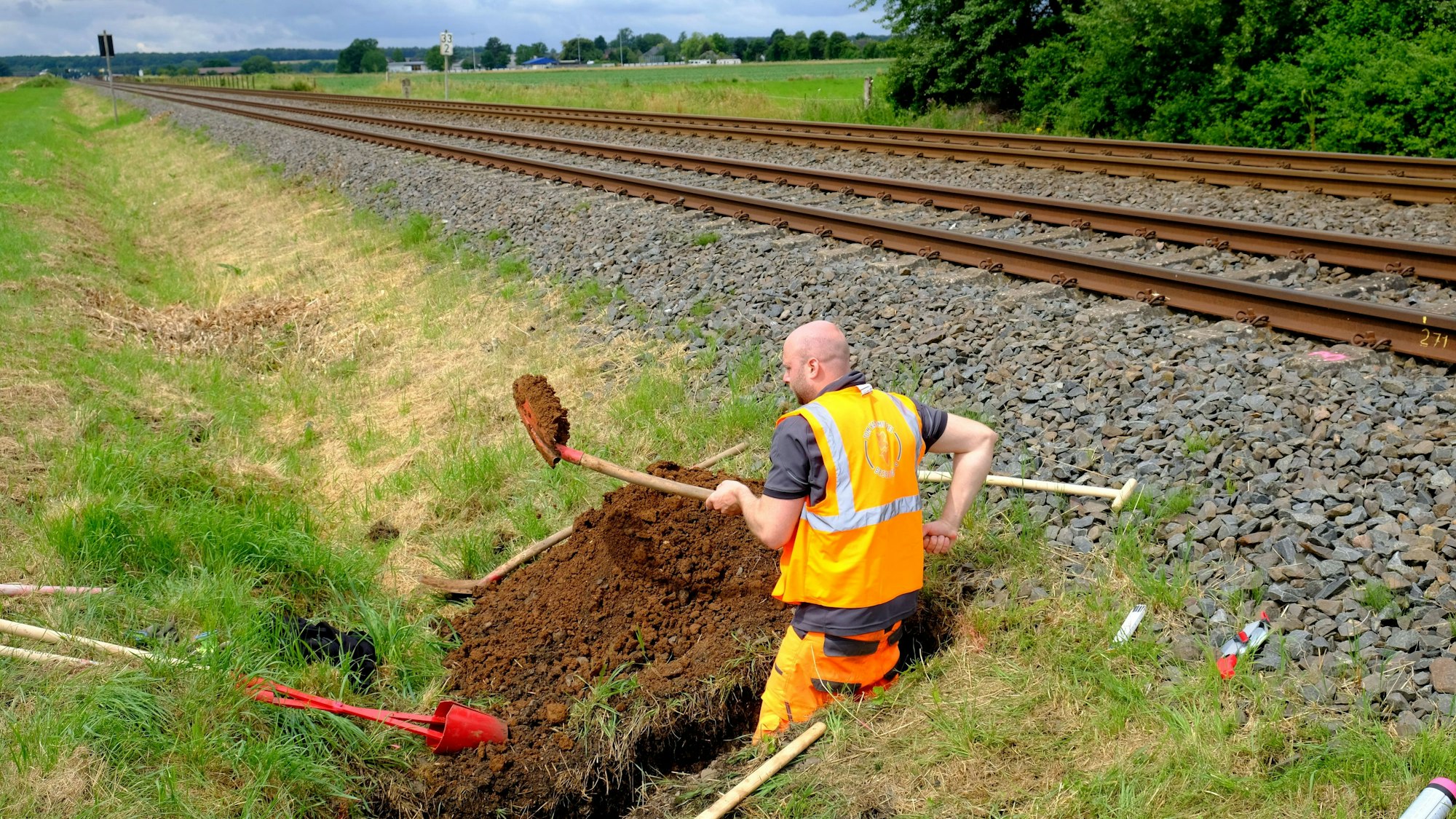 Ein Mann arbeitet mit einer Schaufel neben Bahngleisen.