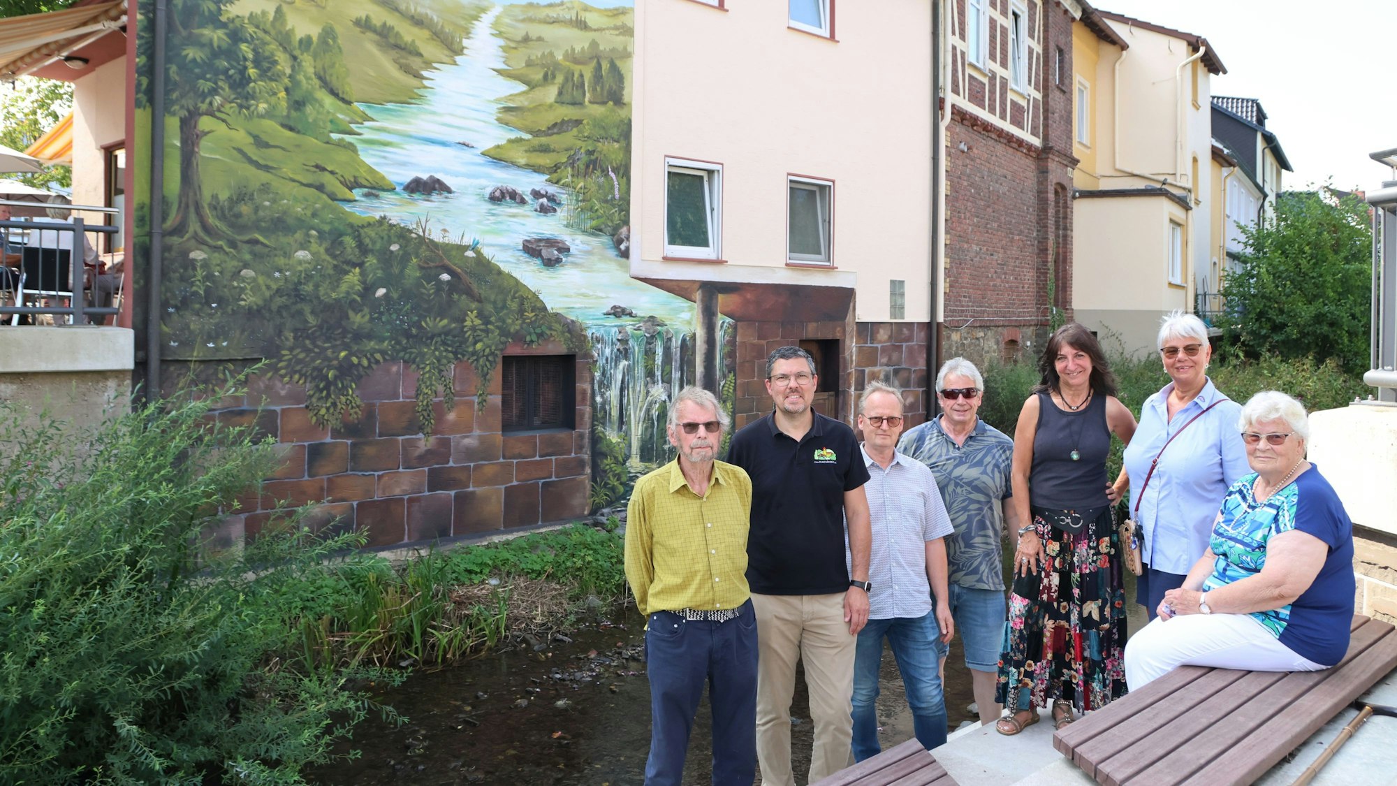 Eine Gruppe steht vor einem Gebäude, auf dessen Fassade ein großes Bild gemalt wurde.