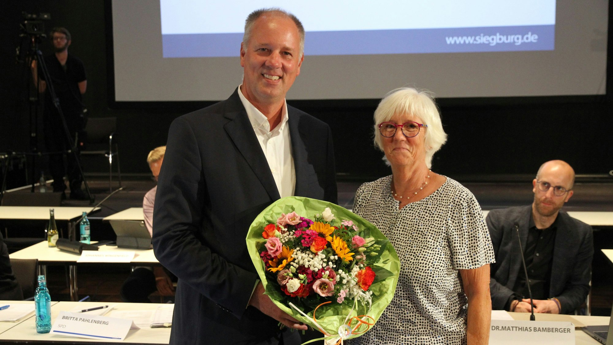 Ein Mann mit einem Blumenstrauß, daneben eine Frau.