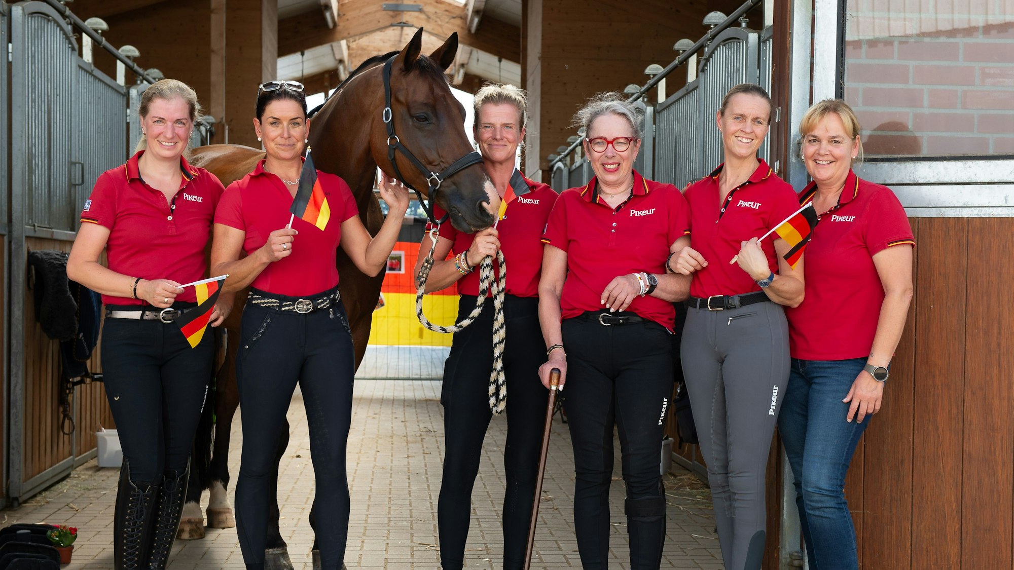 Auf dem Bild ist die deutsche Para-Dressur-Mannschaft mit einem Pferd in der Boxengasse zu sehen.