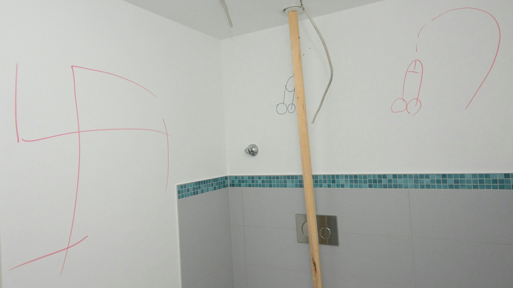 Hakenkreuze und Phallussymbole wurden an die weiße Wand einer Dusche geschmiert.