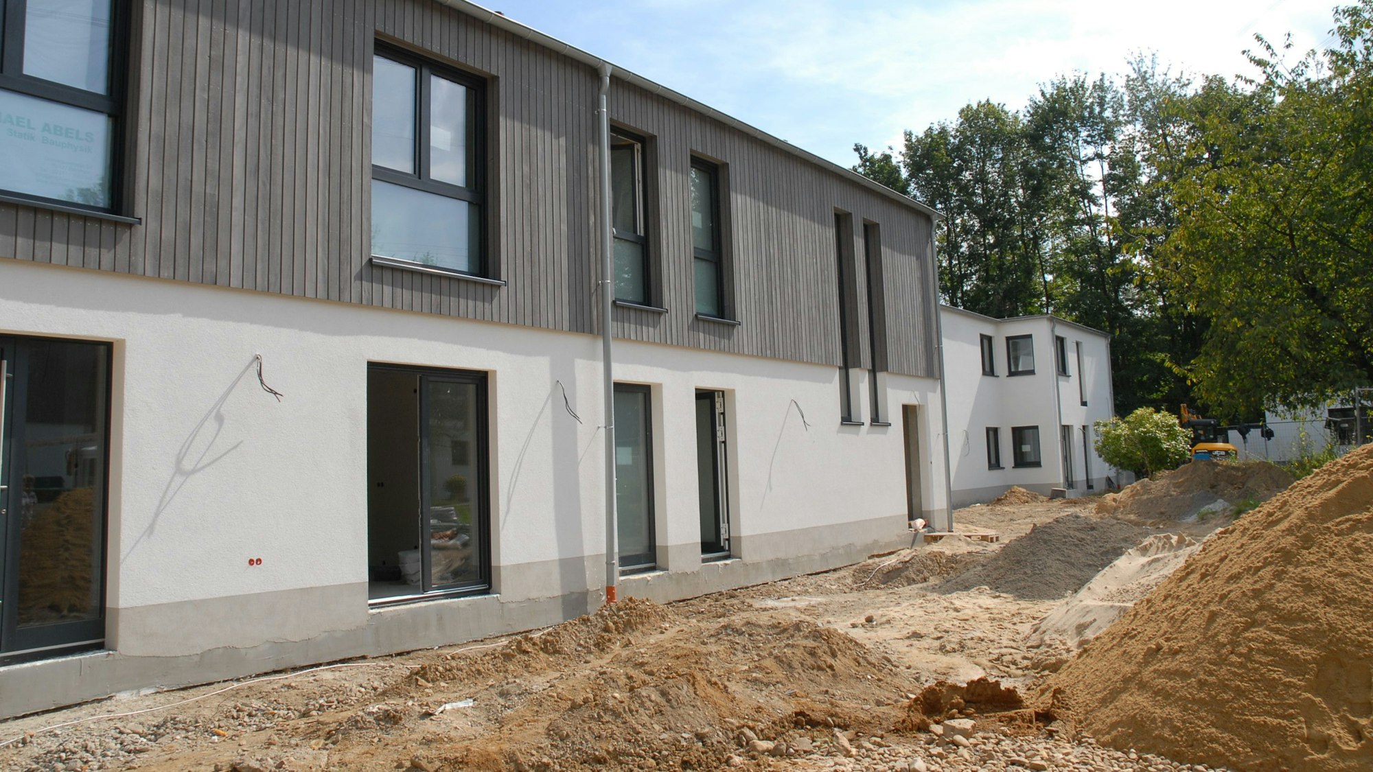 Zu sehen ist ein weißes Gebäude, dessen Obergeschoss mit Holz verkleidet ist.