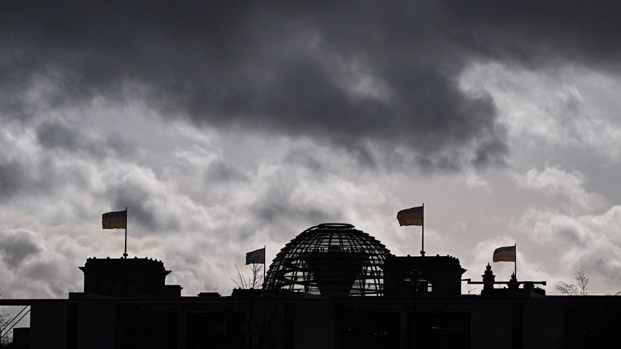 Berlin: Wolken sind über der Kuppel vom Reichstag zu sehen, auf dem Deutschlandfahnen wehen.