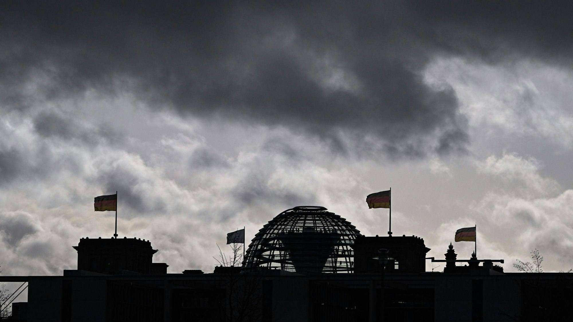 Berlin: Wolken sind über der Kuppel vom Reichstag zu sehen, auf dem Deutschlandfahnen wehen.