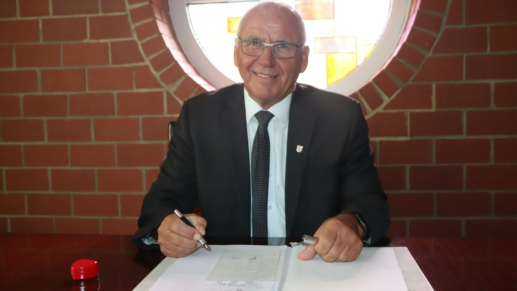 Auf dem Foto ist Helmut Schmitz zu sehen. Er unterschreibt ein Dokument.