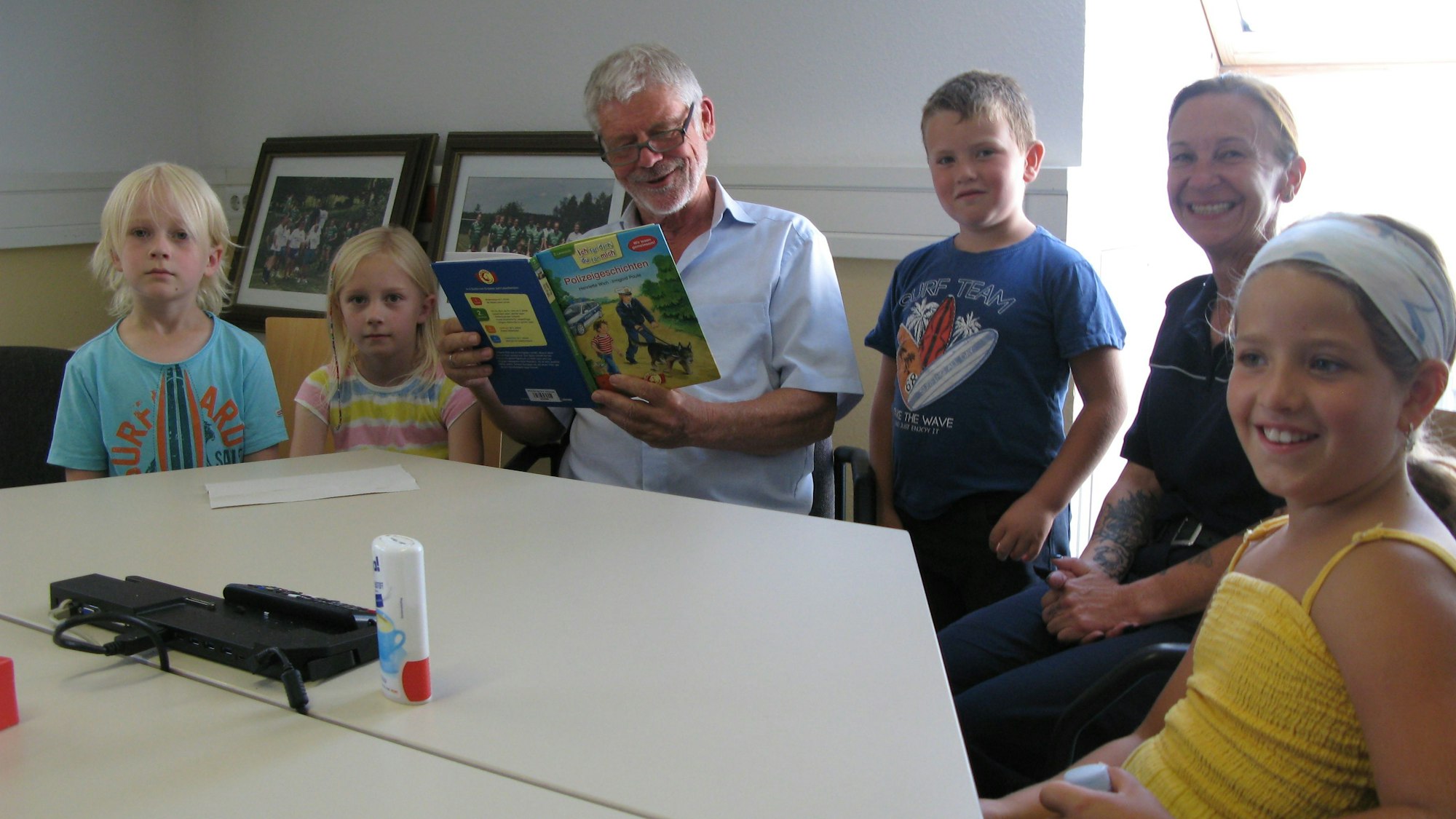 Ein Mann, der ein Buch liest, sitzt umringt von Kindern und einer Frau an einem Tisch.