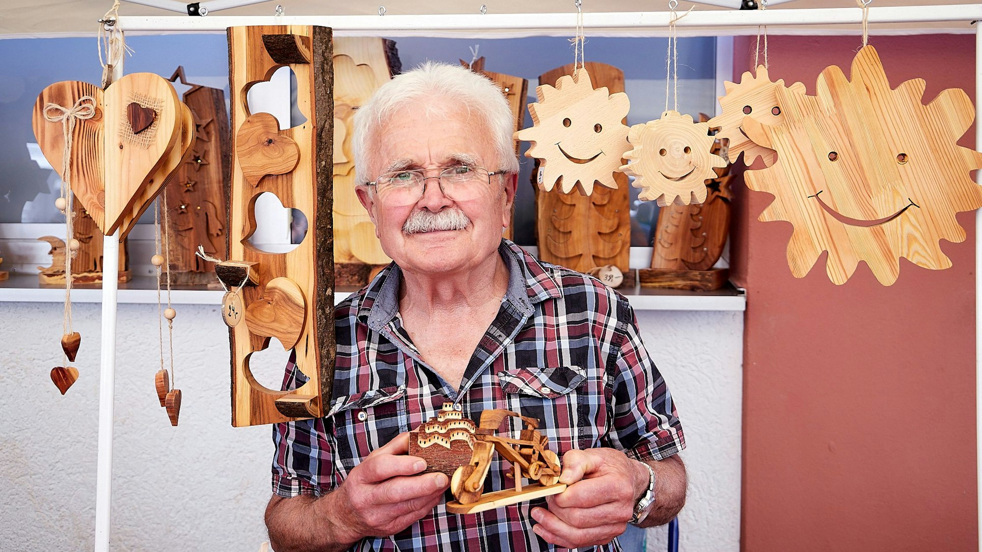 Peter Murges steht zwischen seinen Holzarbeiten, die er aufgehängt hat.