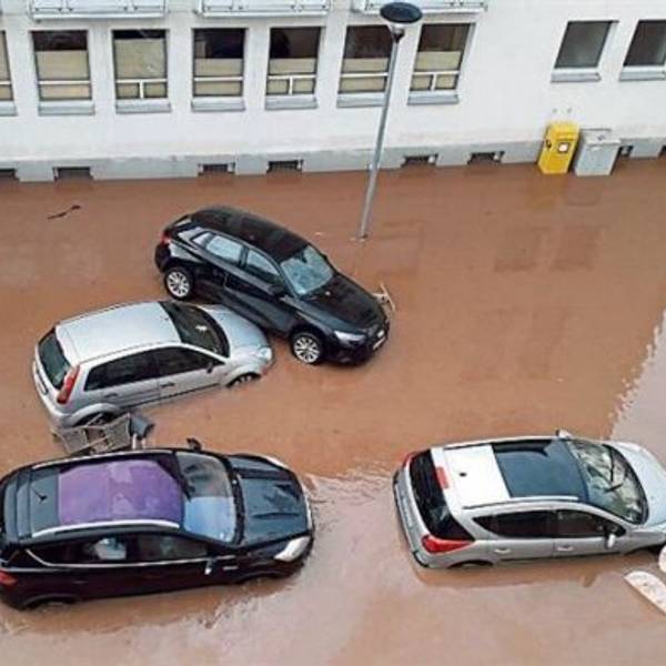 Die Straße ist überflutet. Autos stehen tief im braunen Wasser. Ein Wagen ist auf einen anderen geschoben worden.