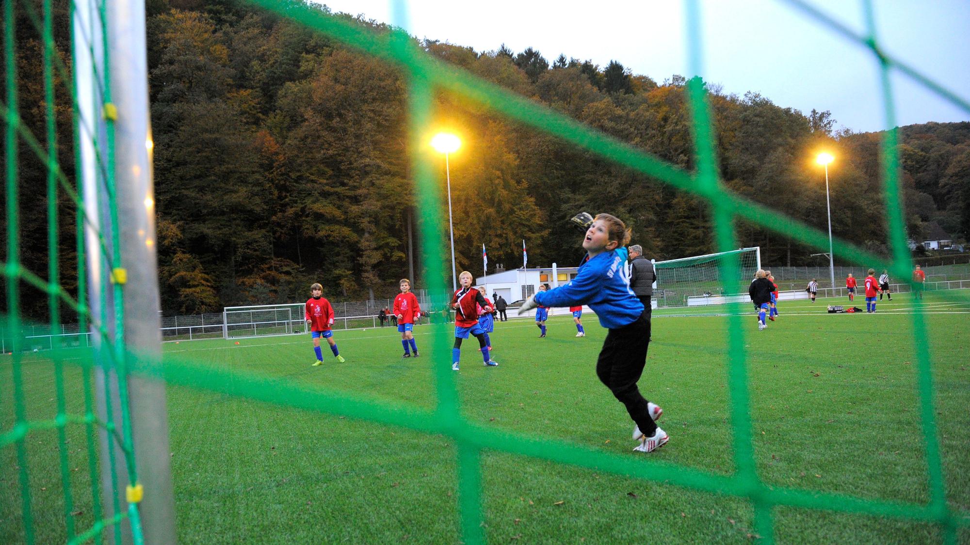 Blick durch das grüne Netz eines Fußballtores auf einen Jungen, der gerade einem Ball hinterherschaut.