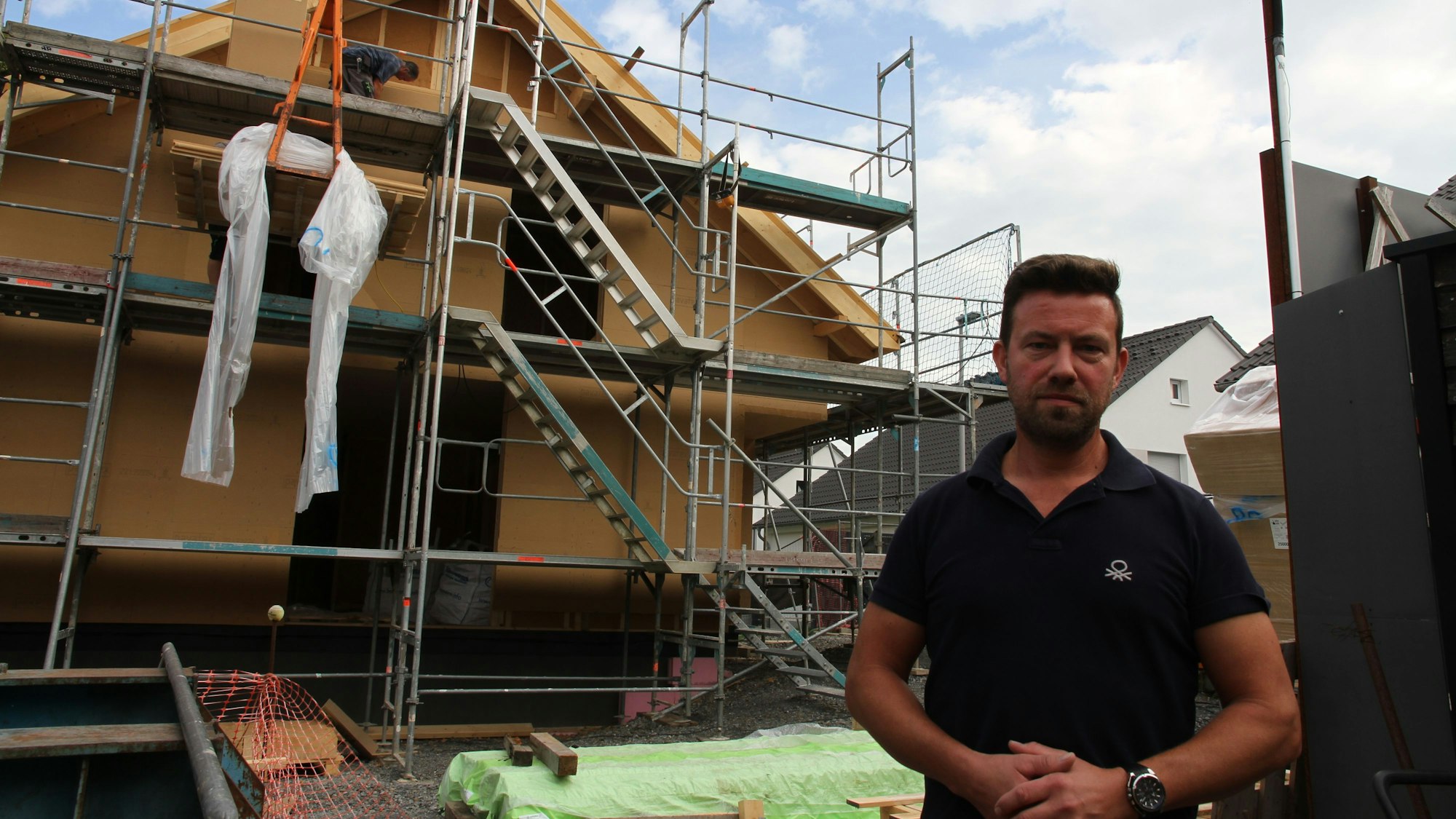 Ein Mann steht vor einem eingerüsteten Rohbau.