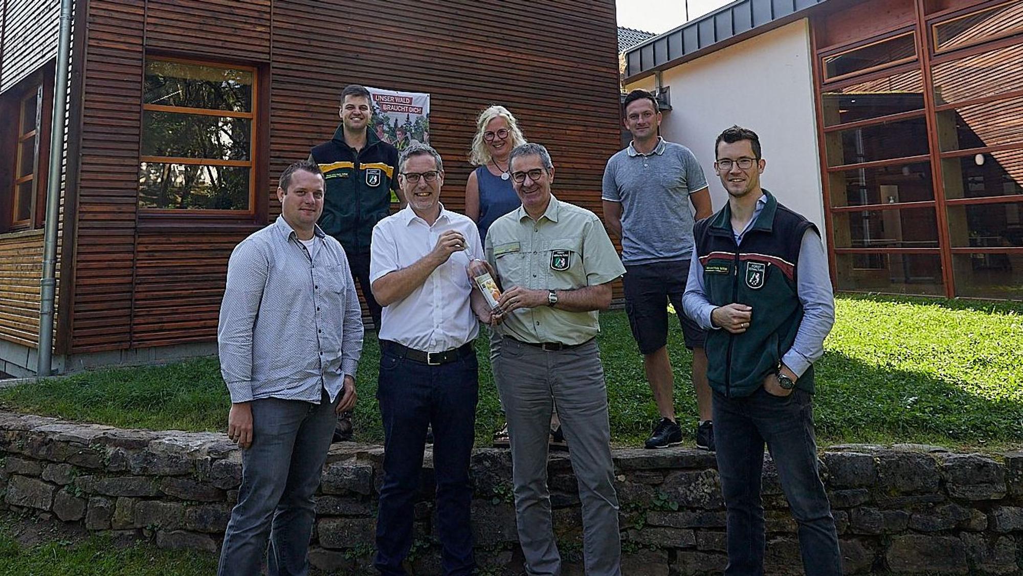Im Kreis von Mitarbeitern des Regionalforstamtes begrüßen Bürgermeister Norbert Crump und Alexander Mauel den Leiter Christoph Böltz zur Wiederkehr der Einrichtung mit einem hochprozentigen Willkommensgeschenk.