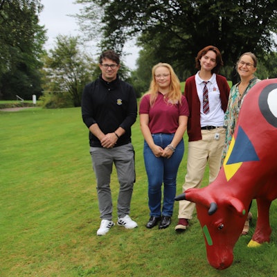 Ein Mann und frei Frauen neben einer bunt bemalten Kuh-Figur