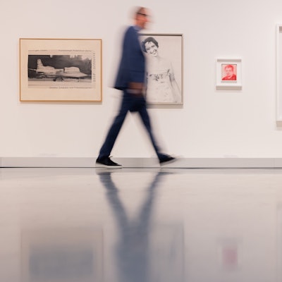 Bilder des Künstlers Gerhard Richter hängen an einer Wand, an der ein Mann vorbeigeht.