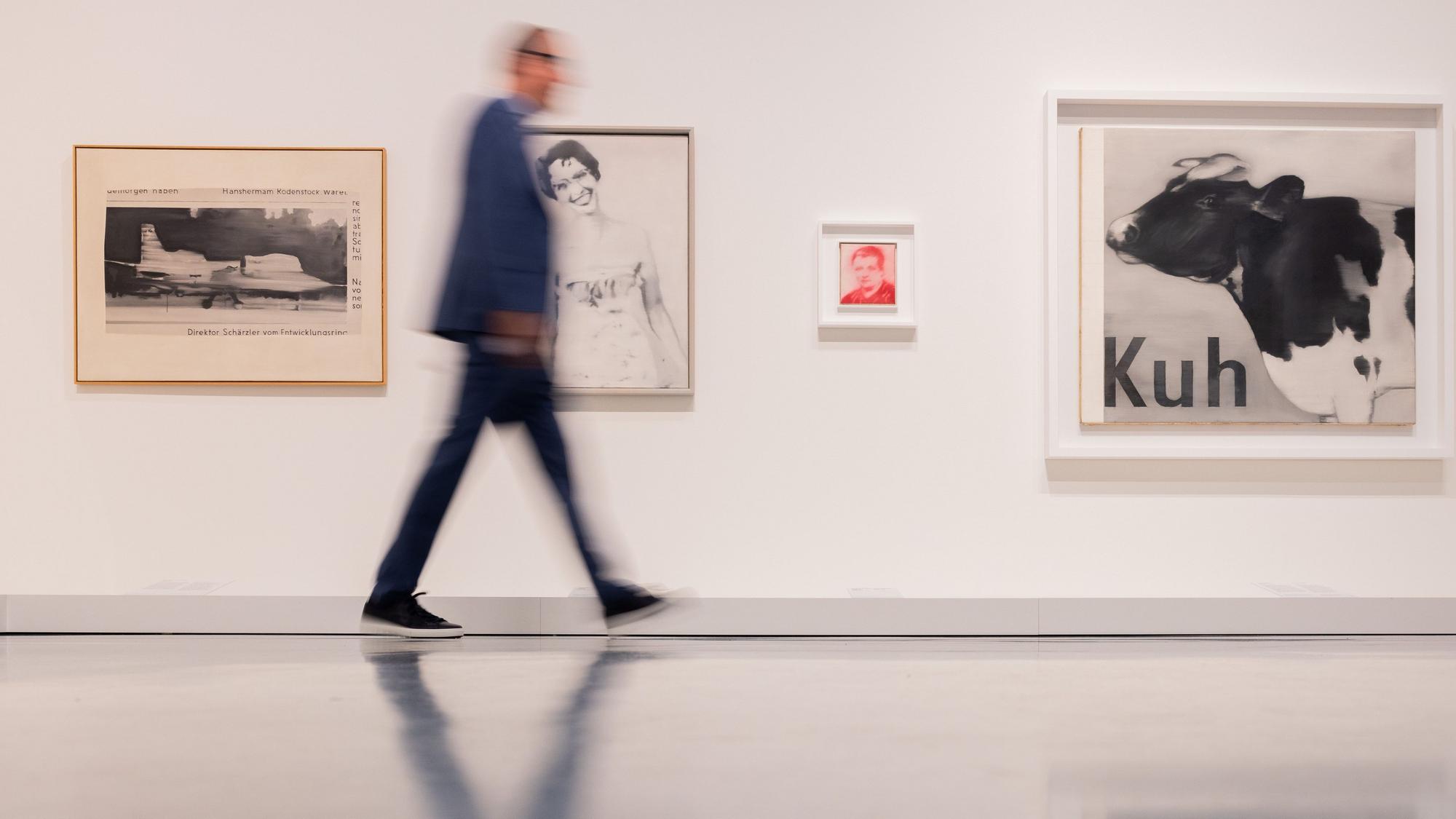 Bilder des Künstlers Gerhard Richter hängen an einer Wand, an der ein Mann vorbeigeht.