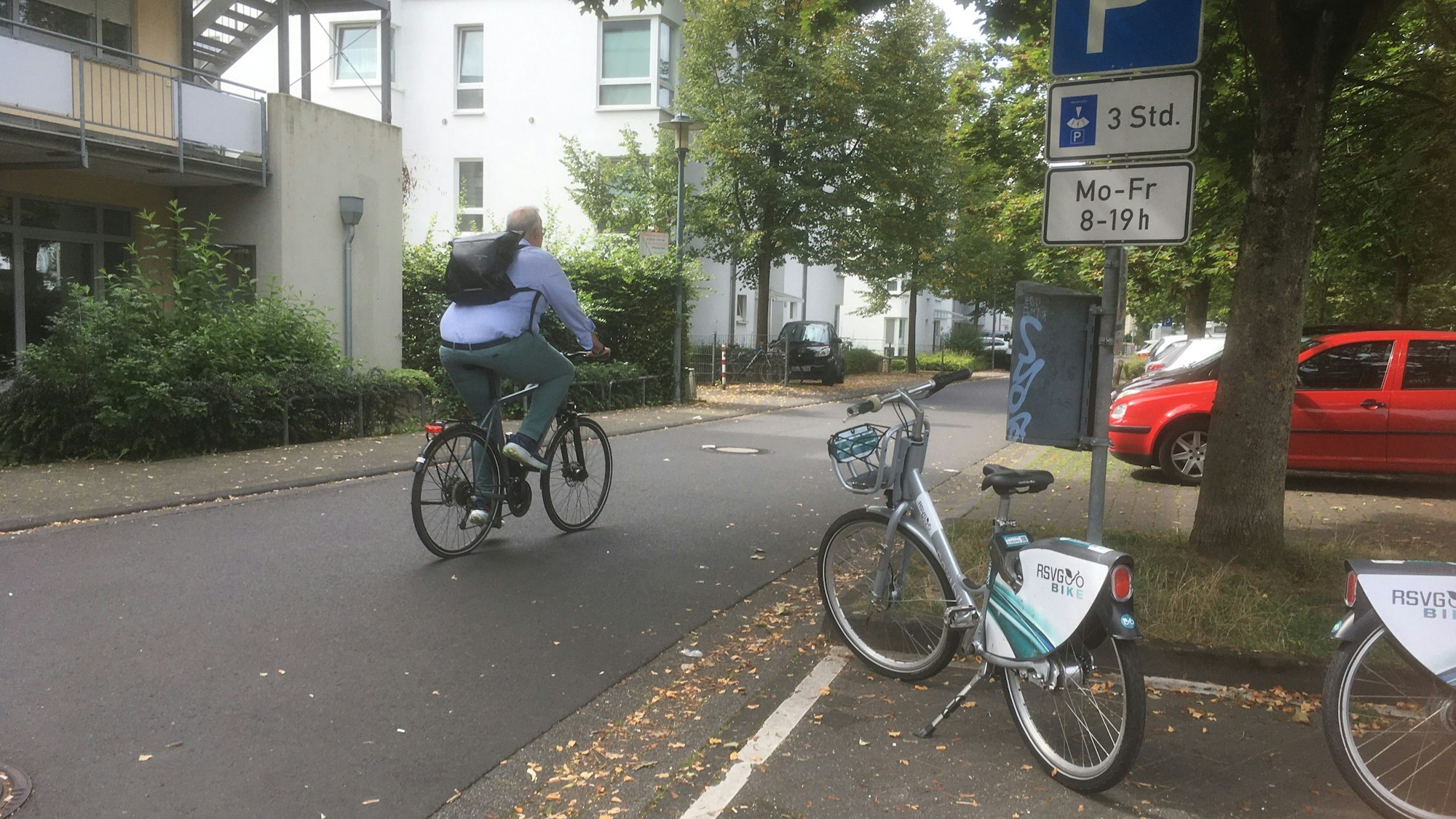 Ein Radfahfrer auf einer innerstädtischen Straße. Rechts stehen Leihfahrräder.