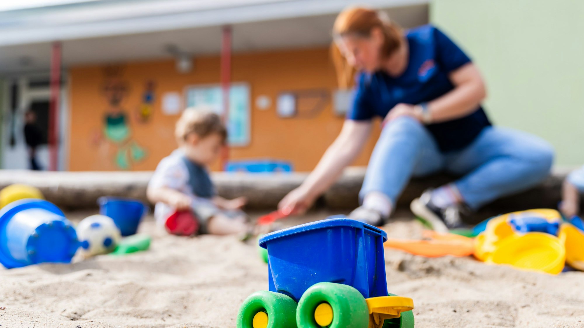 Ein Kind spielt mit einer Erzieherin im Sandkasten einer Kita.