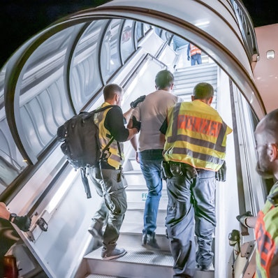 Das Bild zeigt einen Mann, der von Polizisten in ein Flugzeug begleitet wird, damit er mithilfe des Flugs abgeschoben werden kann.