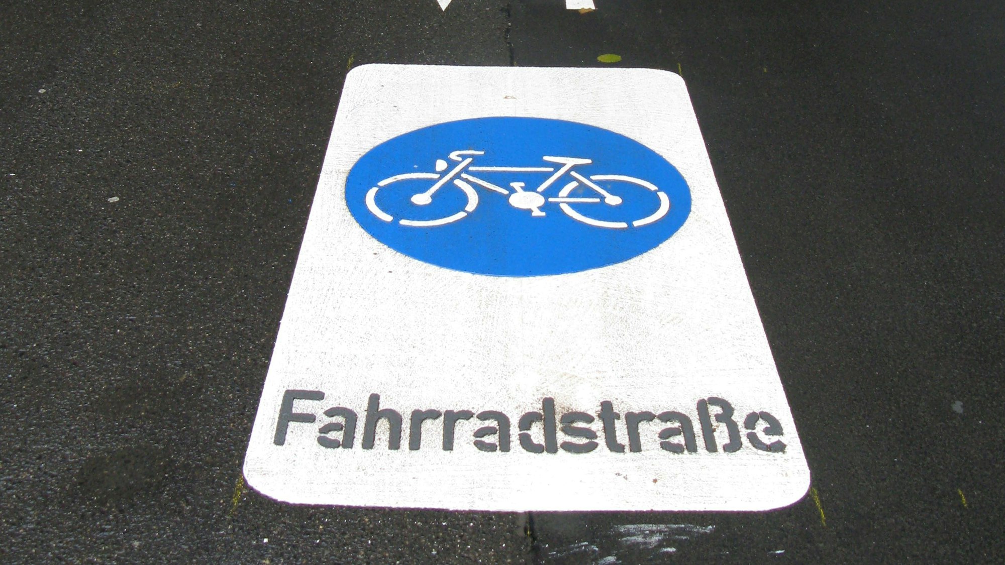 Eine Markierung Fahrradstraße auf einer Straße. In einem blauen Kreis ist ein weißes Fahrrad zu sehen.