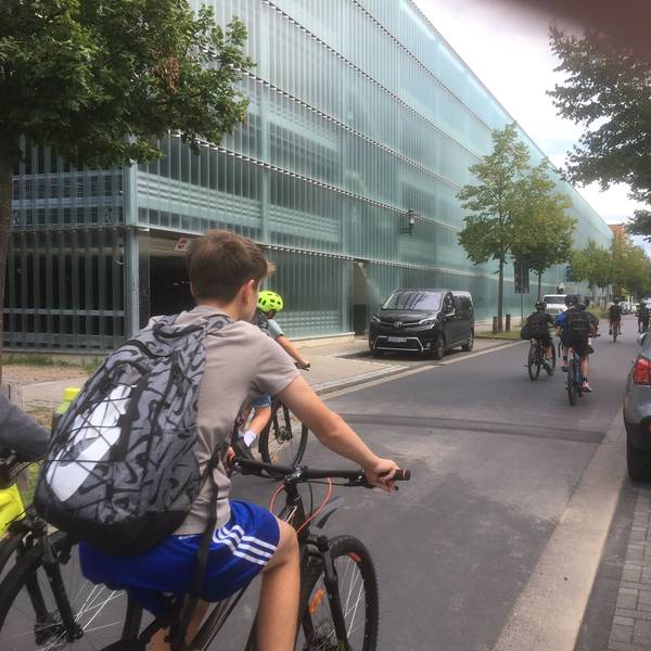 Schüler fahren mit Fahrrädern an einem Parkhaus vorbei.