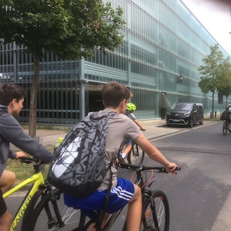 Schüler fahren mit Fahrrädern an einem Parkhaus vorbei.