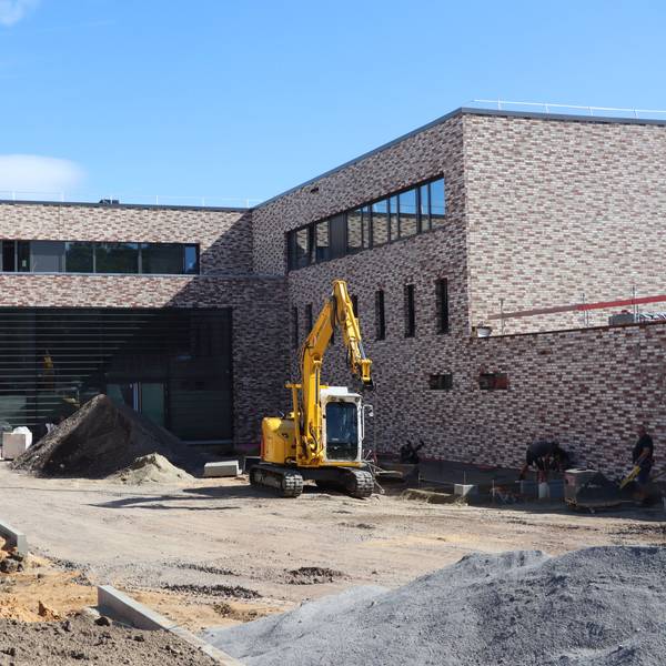 Das Foto zeugt einen Klinkerbau mit großer Fensterfront, davor ein Bagger.