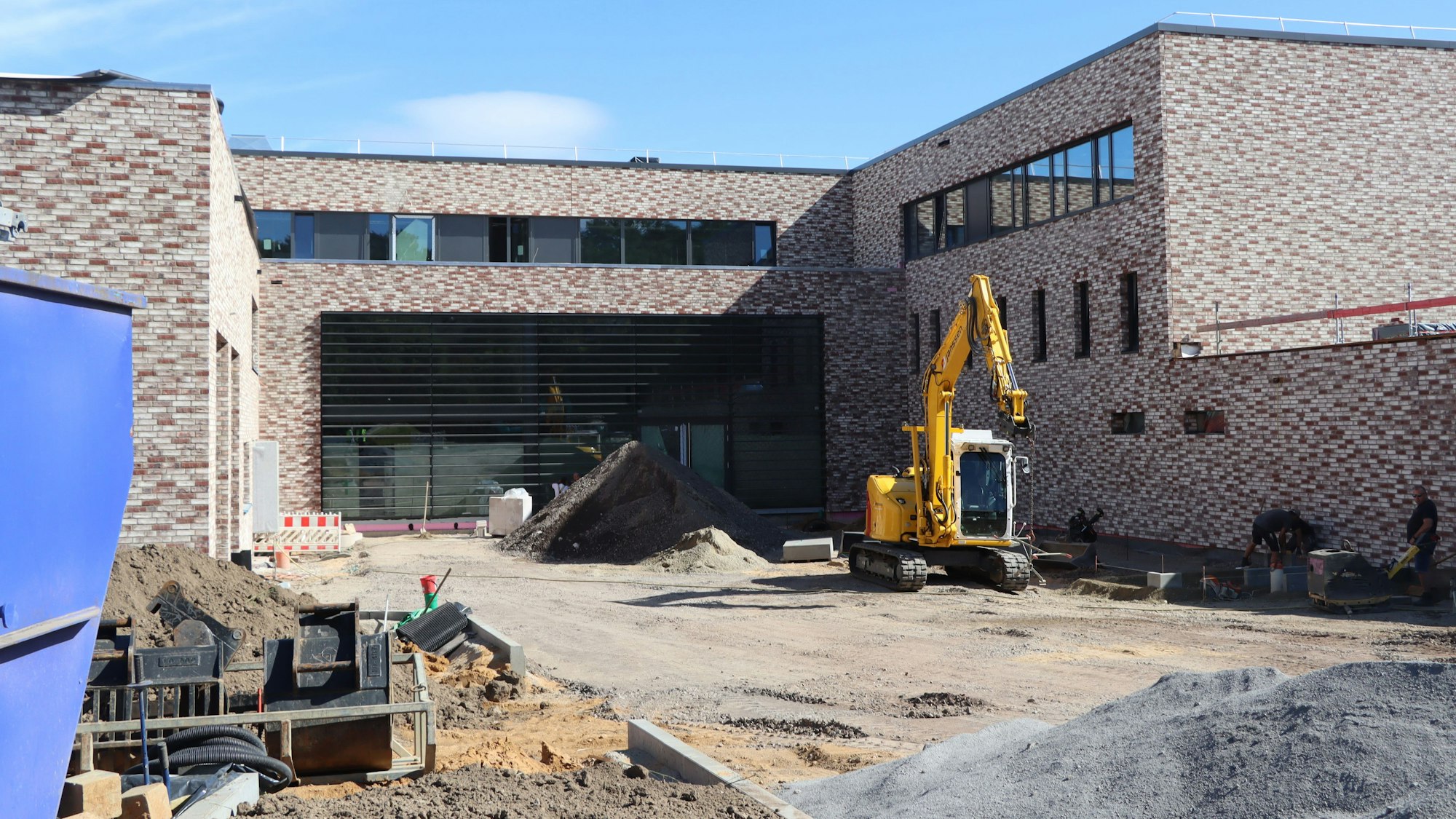 Das Foto zeugt einen Klinkerbau mit großer Fensterfront, davor ein Bagger.