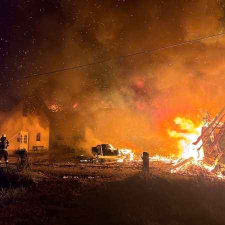 Feuerwehrleute löschen Flammen und bewässern ein Wohngebäude, damit dieses nicht Feuer fängt.