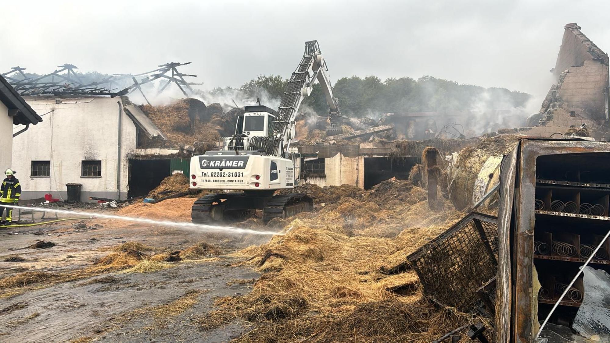 Ein Bagger greift schwelendes Heu aus einem abgebrannten Wirtschaftsgebäudes eines Bauernhofs bei Kürten-Dürscheid.