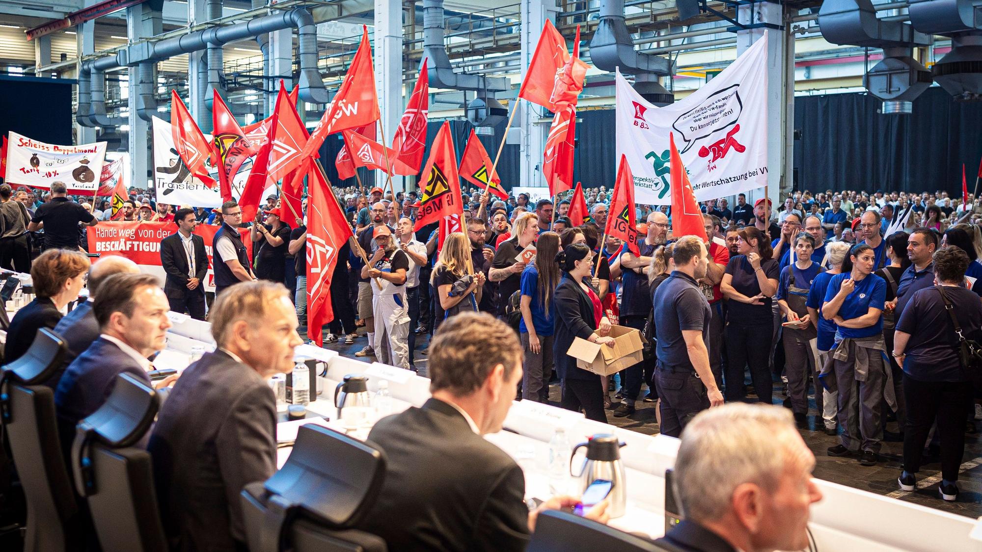 Mitarbeitende protestieren mit Fahnen und Transparenten vor Beginn der Betriebsversammlung von VW.