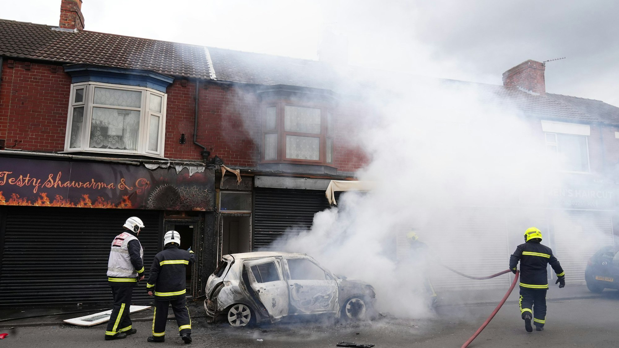 04.08.2024, Großbritannien, Middlesbrough: Feuerwehrleute löschen ein brennendes Auto in der Parliament Road in Middlesbrough während einer Anti-Einwanderungsdemonstration.