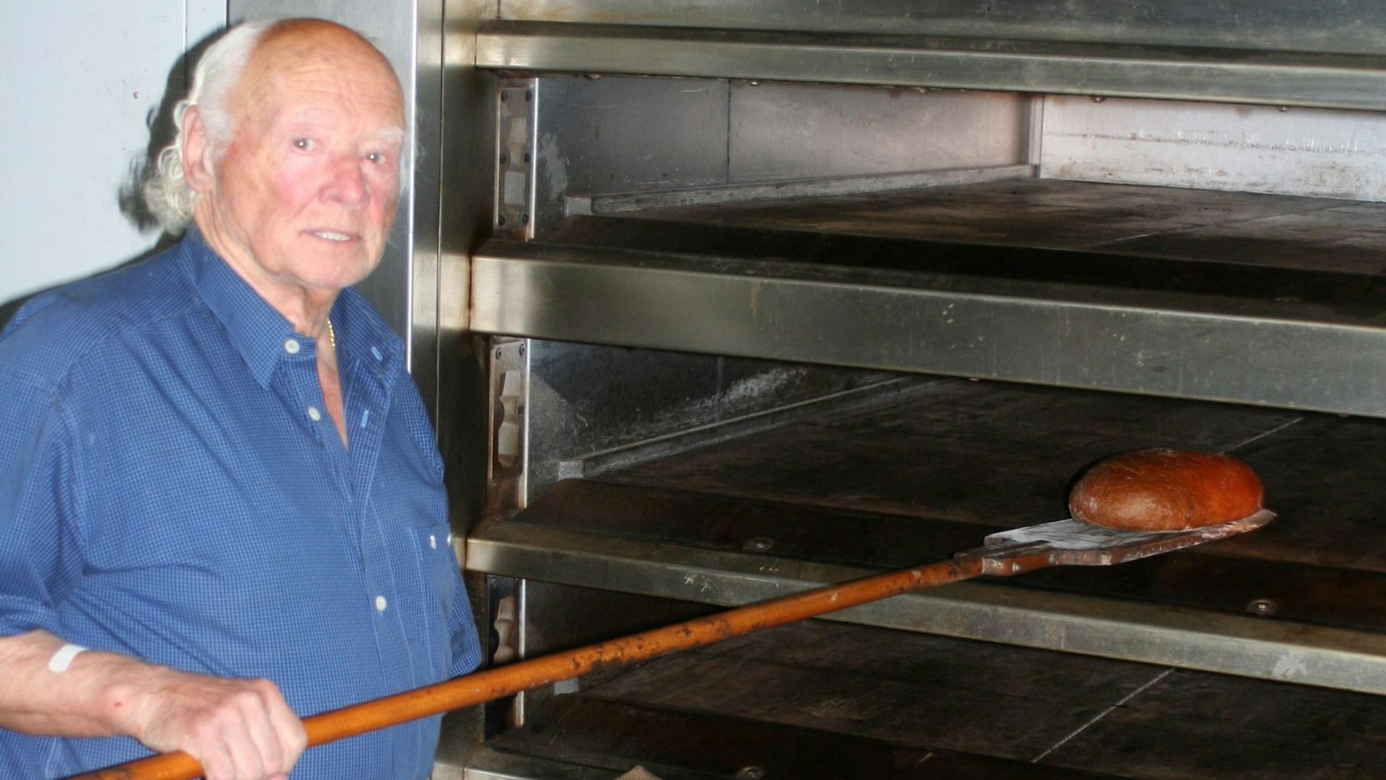 Ein Mann steht am Backofen und holt ein Brot heraus.