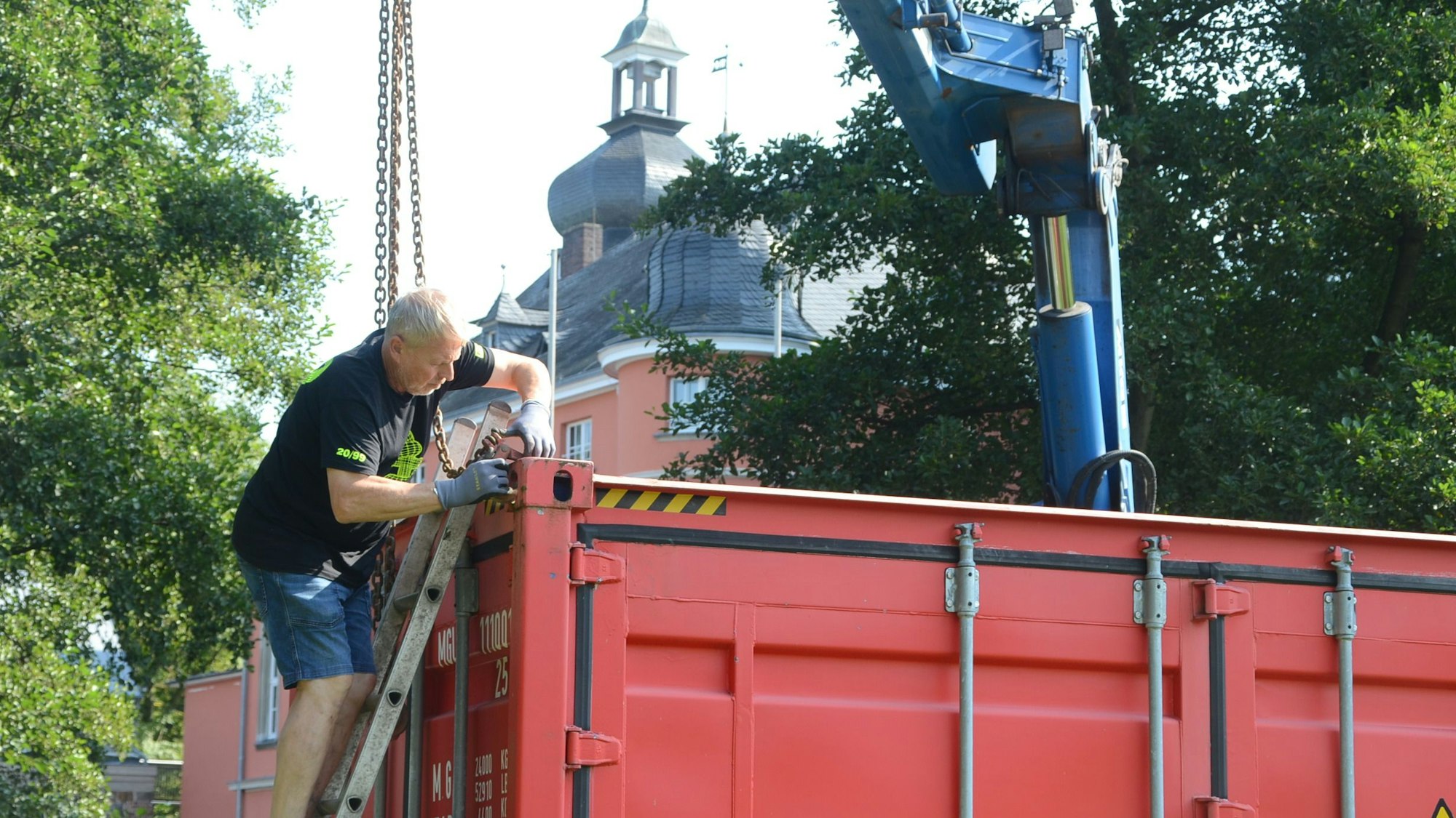 Ein Mann befestigt Metalltrossen an einem roten Überseecontainer.