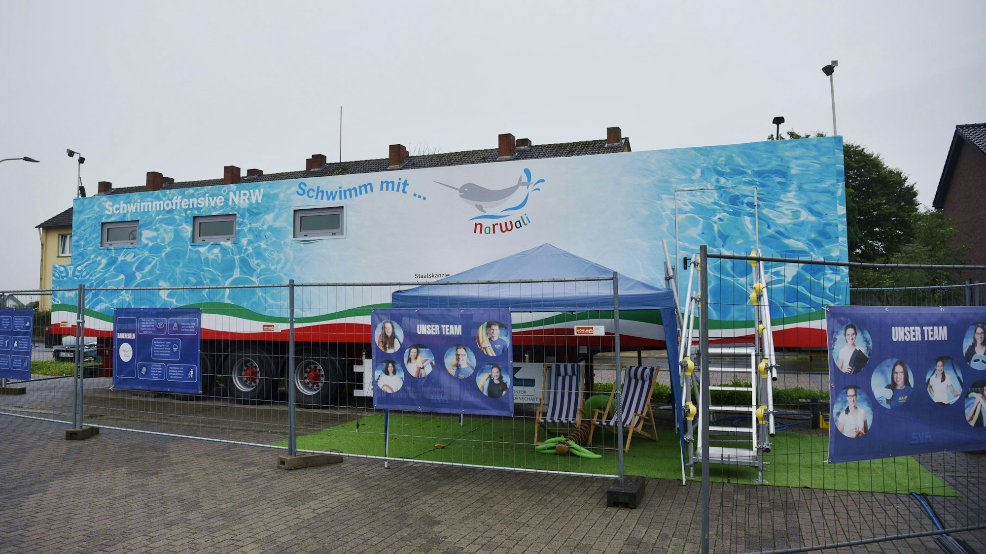 Das Bild zeigt einen umgebauten Überseecontainer. Er befindet sich auf einem Lkw-Auflieger und beinhaltet ein Lehrschwimmbecken.