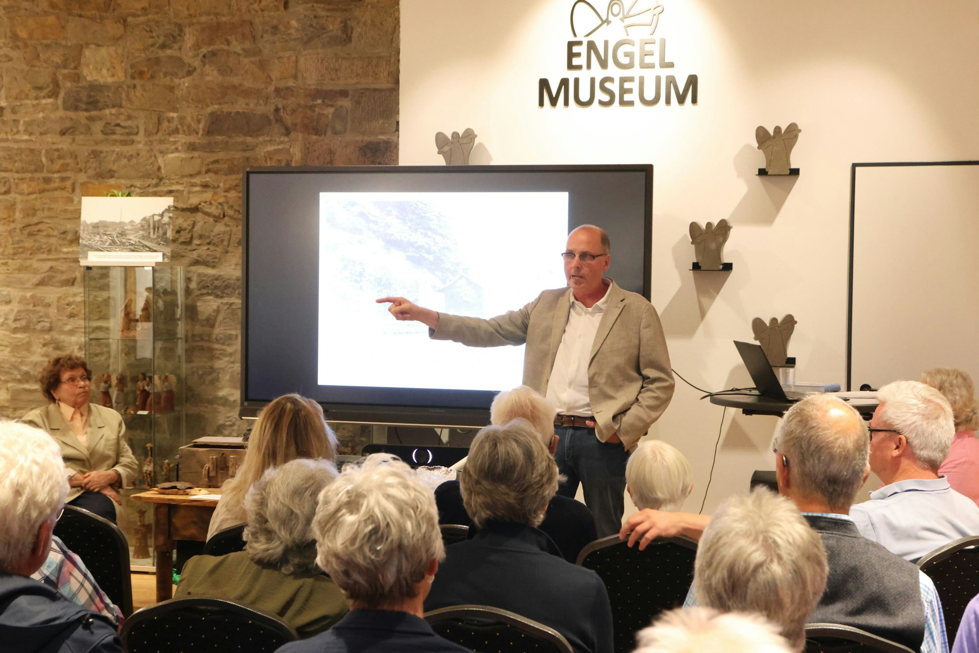 Uwe Bathe steht vor einer Gruppe Menschen und zeigt in Richtung eines Bildschirms.