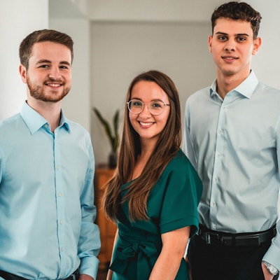 Zu sehen sind zwei junge Männer und eine junge Frau (Mitte).