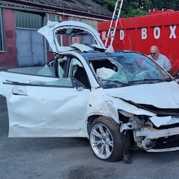 Ein Schrottauto steht neben einem offenen Container.
