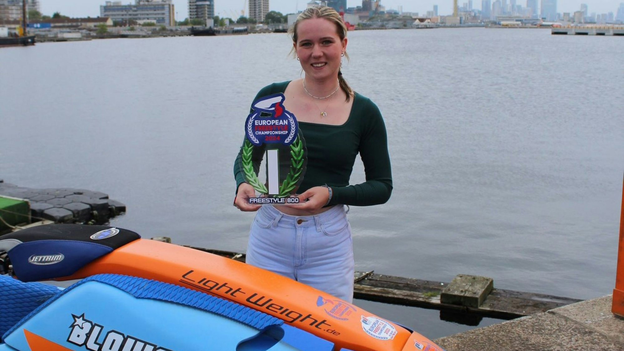 Bild einer jungen Frau, die mit einem Pokal am Rand eines Hafensbeckens steht