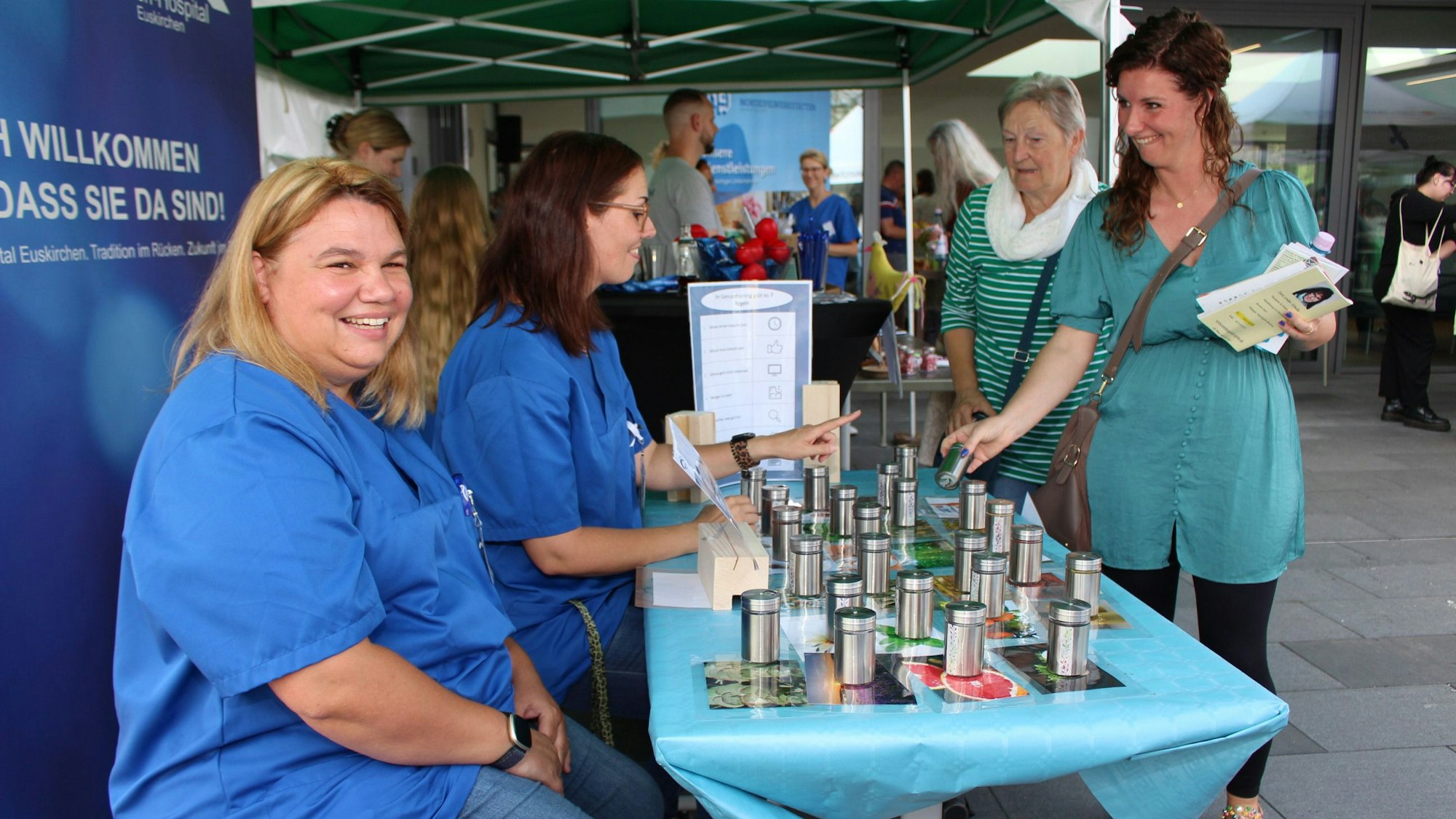 An einem Tisch sitzen zwei lachende Frauen, während eine weitere Frau gut gelaunt nach einem Gegenstand auf dem Tisch greift.