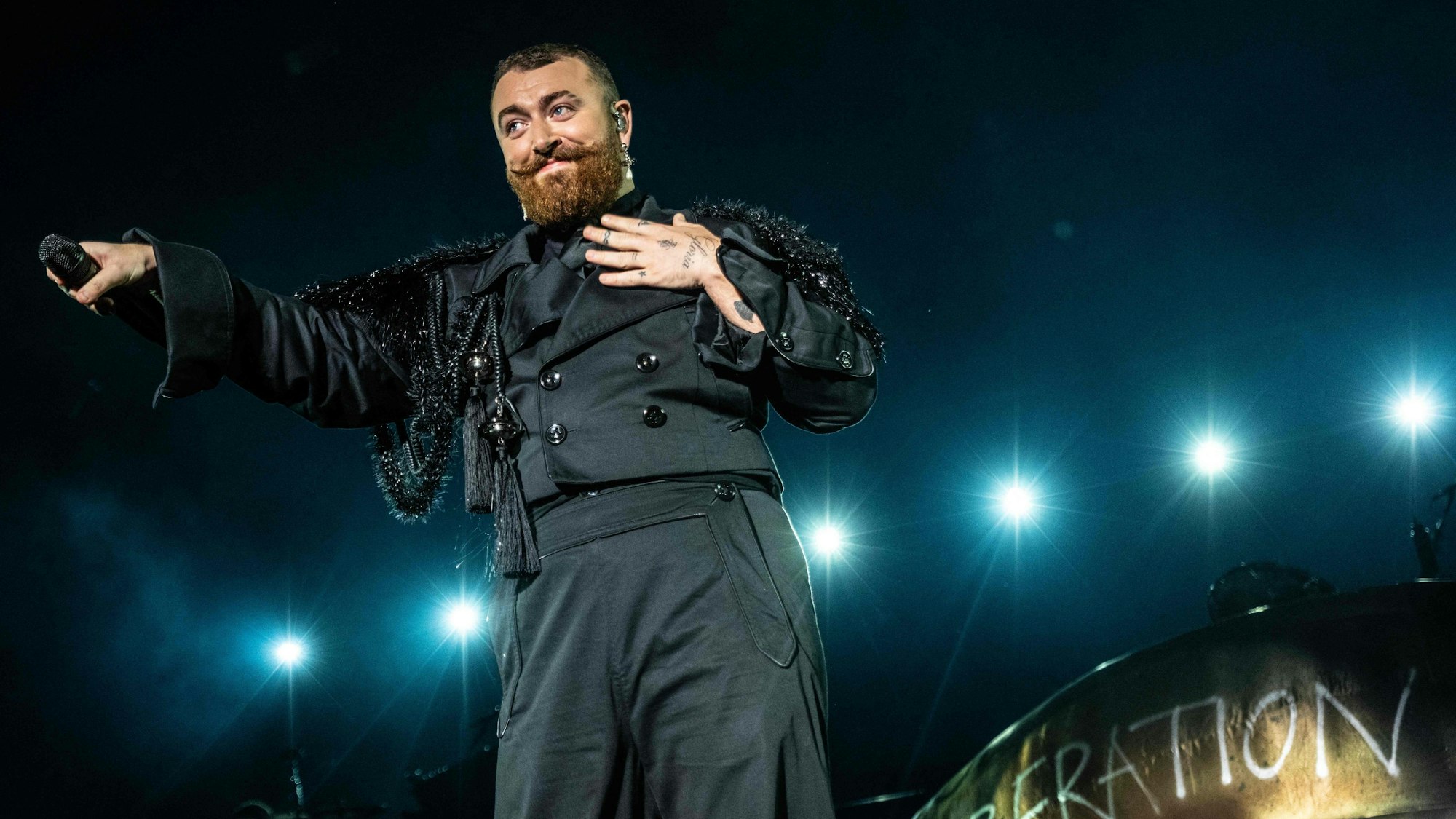 Sam Smith steht auf der Bühne und hält ein Mikrofon ins Publikum.