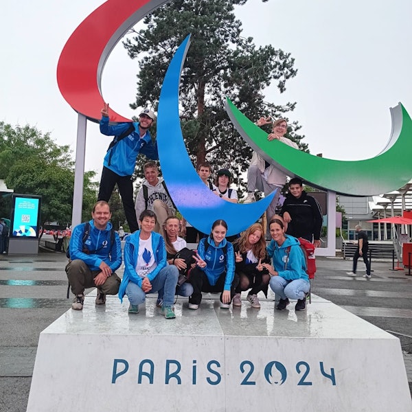 Eine Schülergruppe und ihre Betreuer stellen sich zu einem Gruppenfoto an einer Statue der Paralympischen Spiele mit der Aufschrift „Paris 2024“ zusammen.