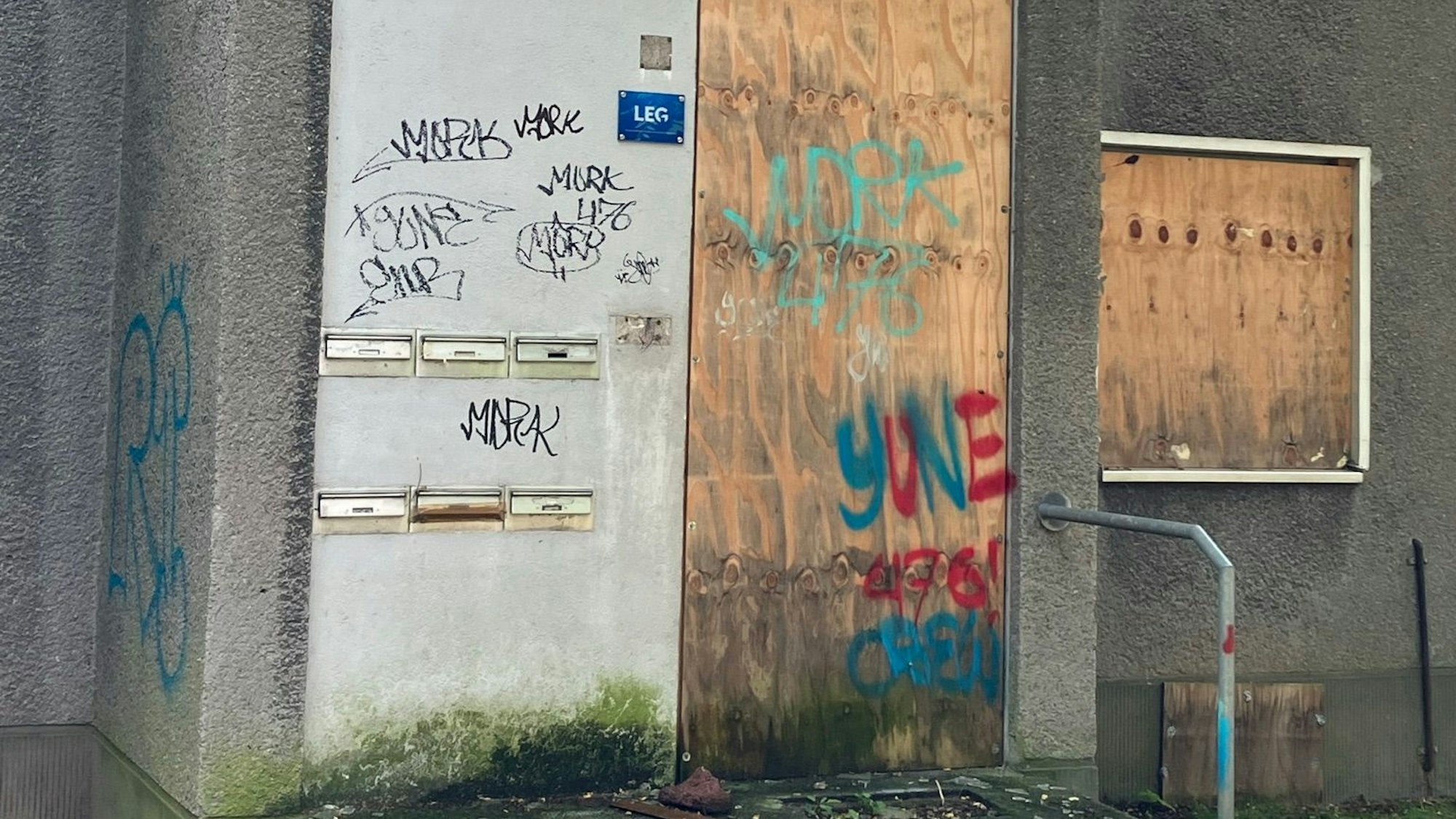 Zu sehen sind verbretterte Fenster und Türen sowie Graffiti-Beschmierungen an den Wohnhäusern um den Schlebuscher Weg.