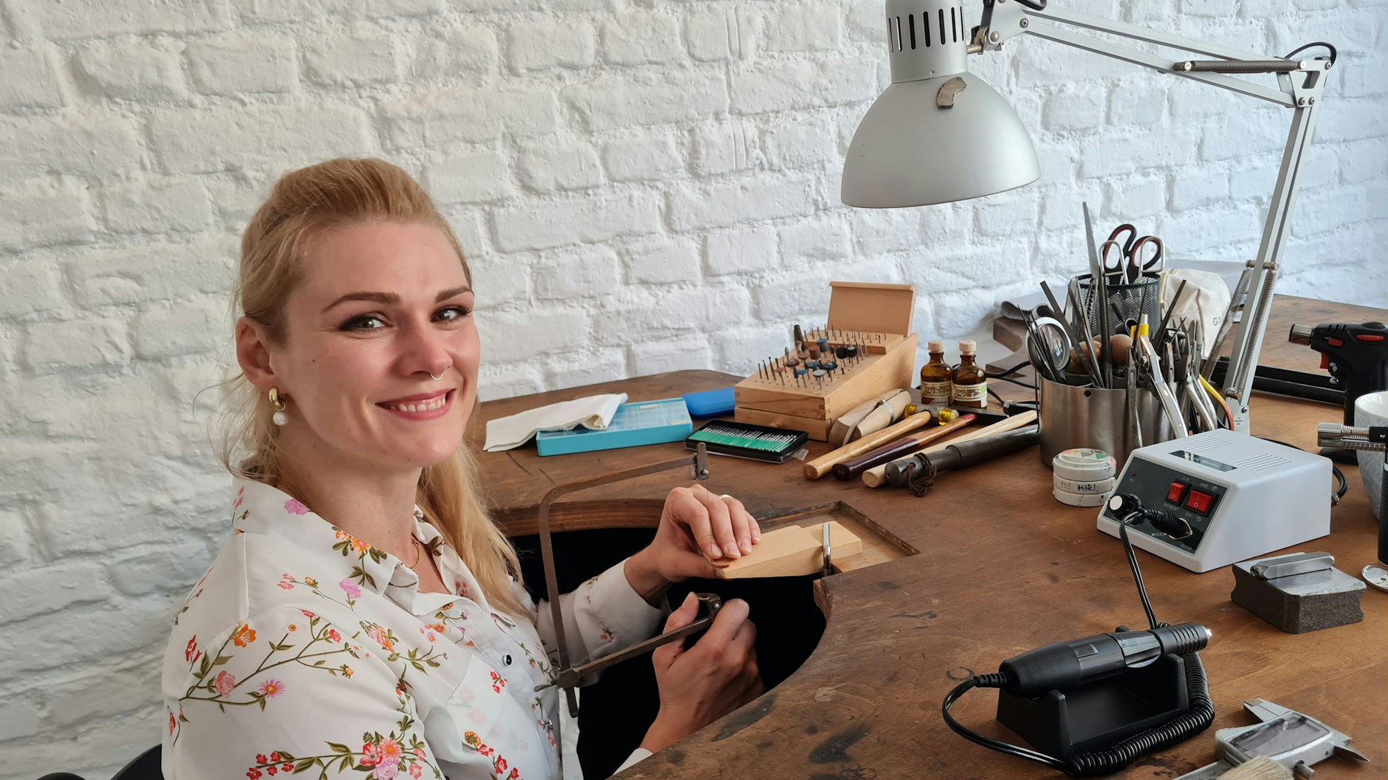 Sabrina Schildgen sitzt an einem Werktisch und zeigt eine kleine Säge.