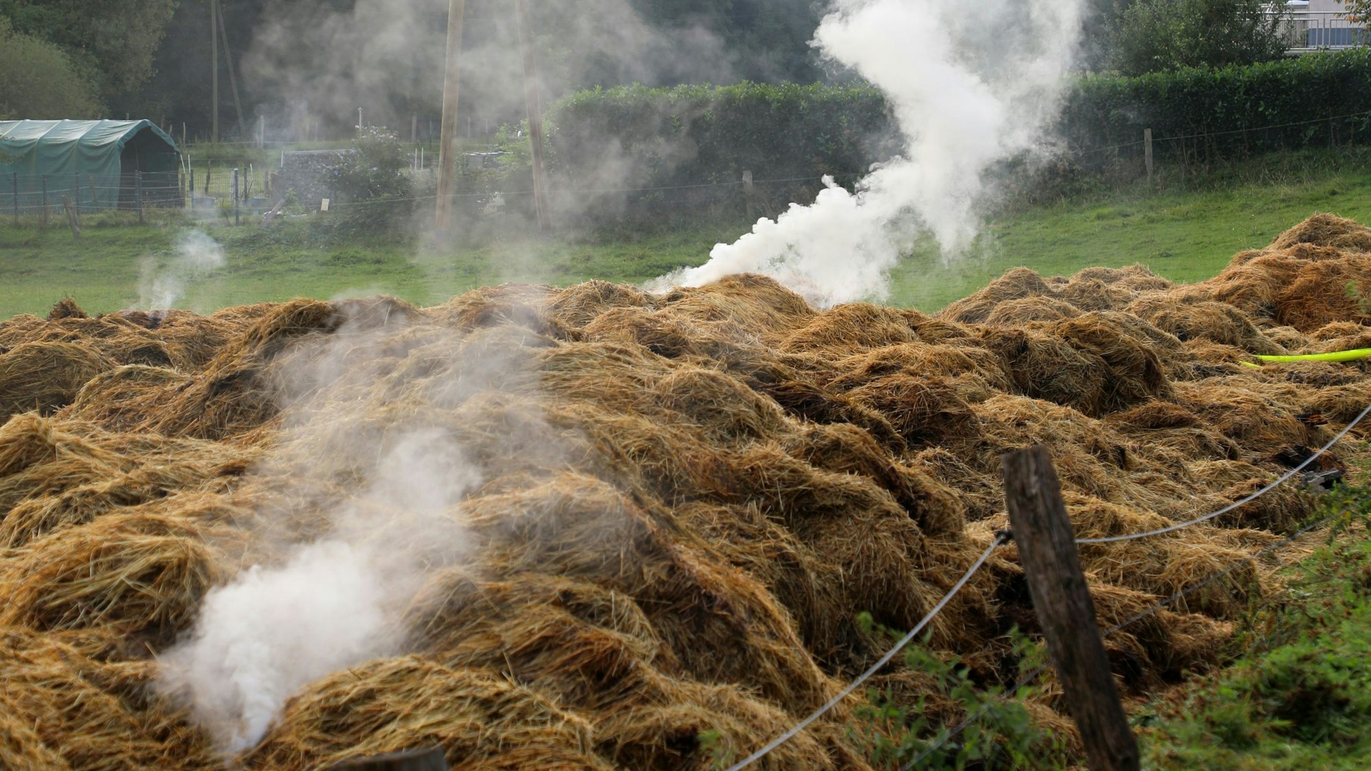 Aus Heuhaufen auf einer Wiese steigt Rauch auf.