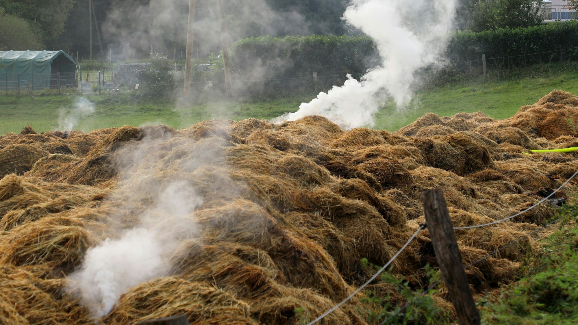 Aus Heuhaufen auf einer Wiese steigt Rauch auf.