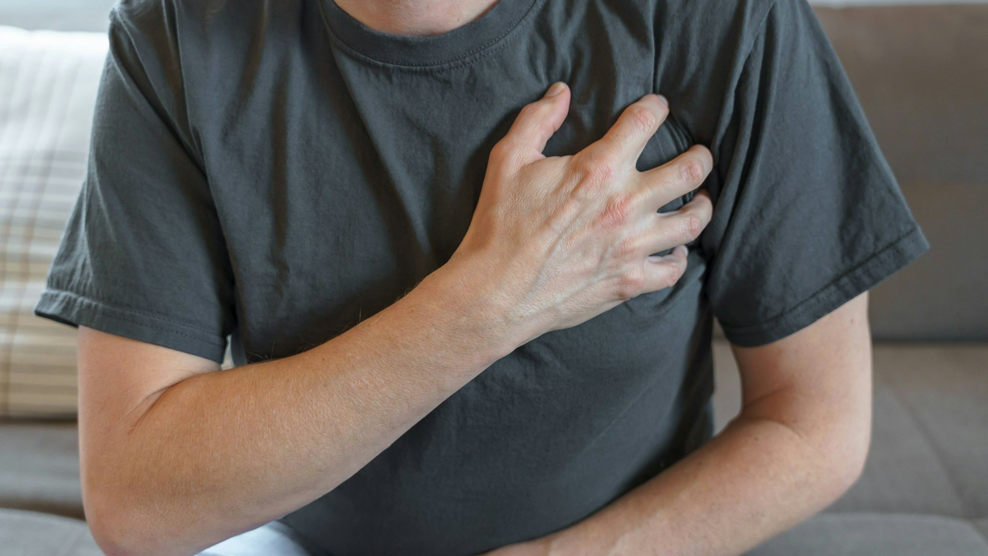 Ein Mann sitzt auf einem Sofa und hält sich die Brust