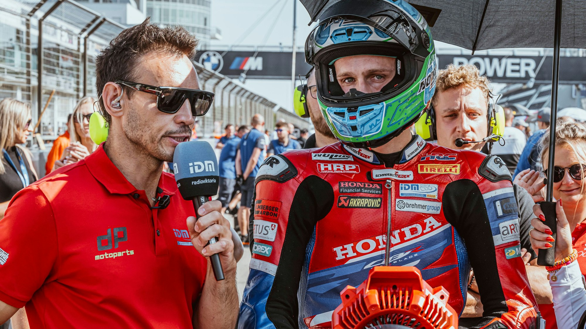 Zu sehen ist, wie ein Reporter einen Motorradrennfahrer per Mikrofon interviewt.